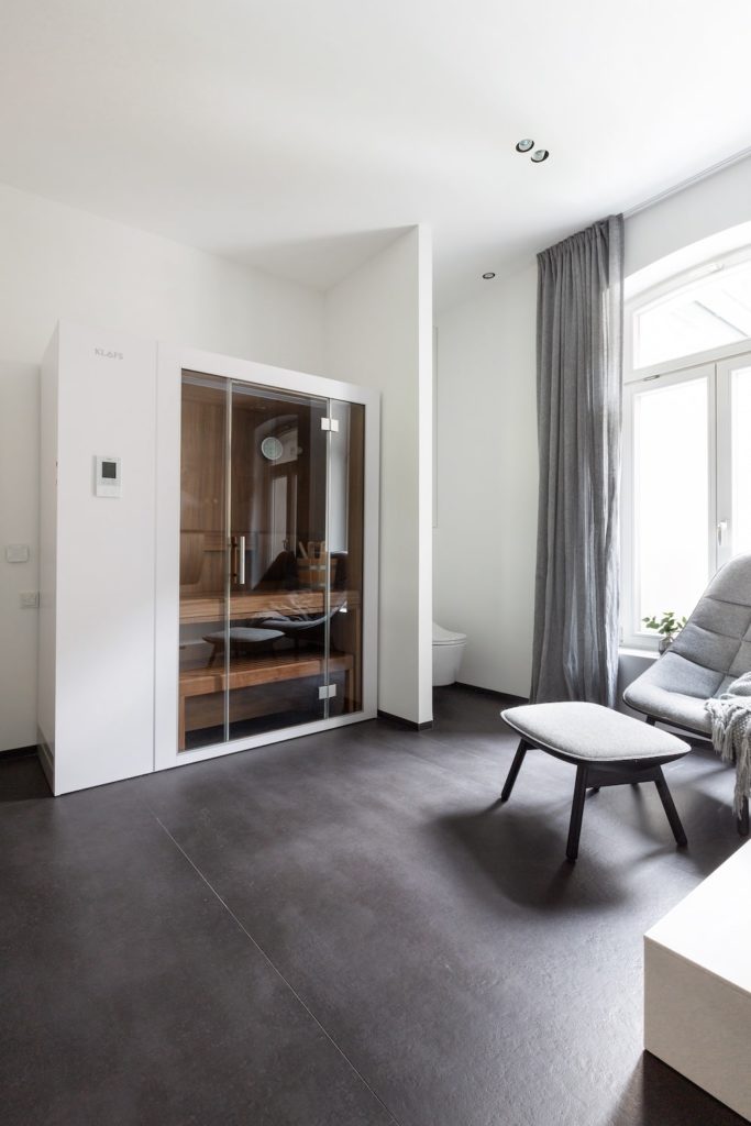 Kleine Sauna welche auf Maß angepasst werden kann neben einem Lounge Chair von Dedon. Bodenbelag aus großformatigen Designer Fliesen.