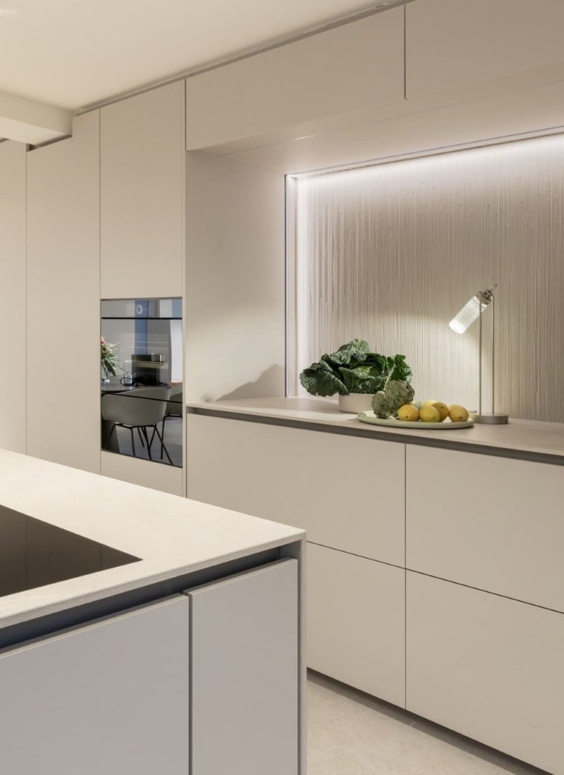 Moderne Küche mit minimalistischen weißen Schränken, einer Arbeitsplatte mit grünen Blättern, Limetten und Zitronen und einer modernen Lampe unter der Einbauleuchte. | casaceramica