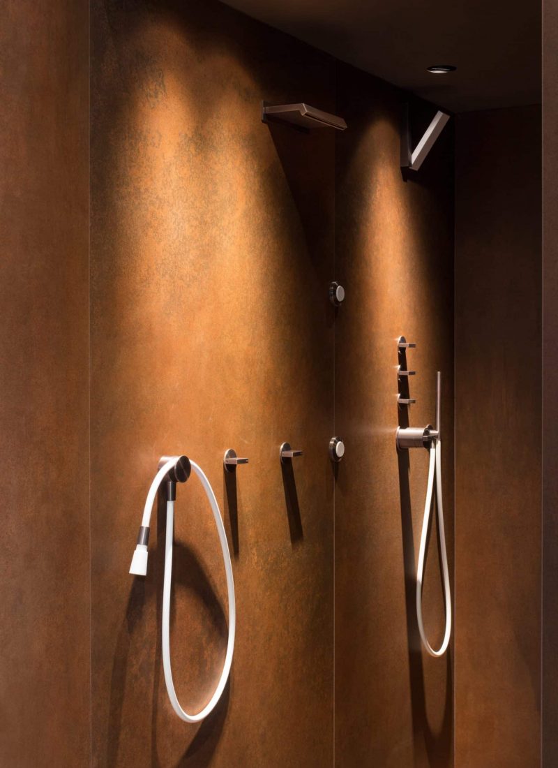 Verschiedene Wellnessarmaturen in Weiß und Kupfer. Die Armaturen sind auf einer Cortenoptik Fliese angebracht.
