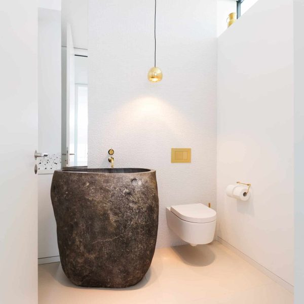 Braunes Natursteinwaschbecken neben WC mit goldenen Armaturen