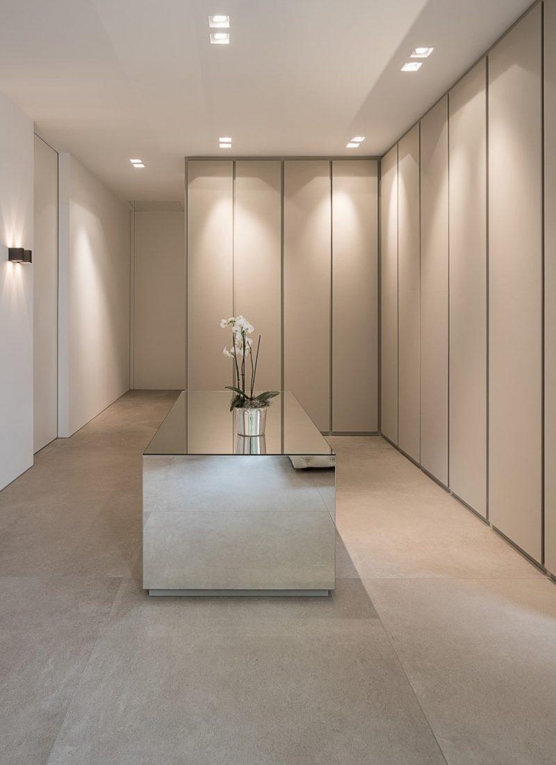 Großzügiges Ankleidezimmer mit deckenhohen Einbauschränken, Boden aus Designer Feinsteinzeug in Natursteinoptik und verspiegelter Mittelinsel